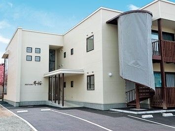 ２階建ての建物は日当たり良好で白い外壁。敷地内には広い駐車場があり、屋外階段もある。