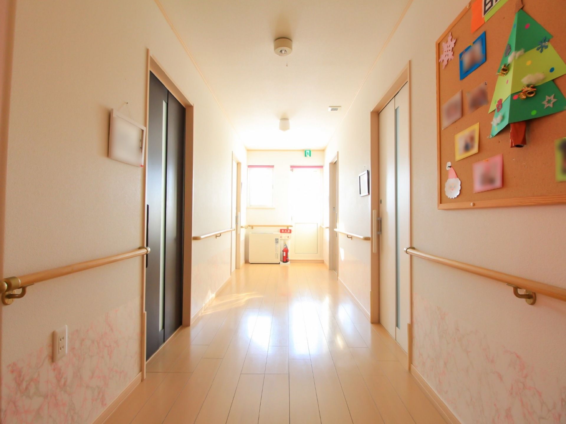 廊下の幅は広く、突き当りの窓からは光が差し込み明るい。両側に手すりが付けてあり、掲示板にはクリスマスの飾りと写真が掲示されている。