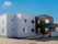 ライトグレーとブラウンの2階建ての建物の玄関には手すり付きのスロープがあり、屋根も付いている。