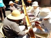 そうめん流しを楽しんでいる入居者。みな帽子をかぶって竹の両サイドに座っている。