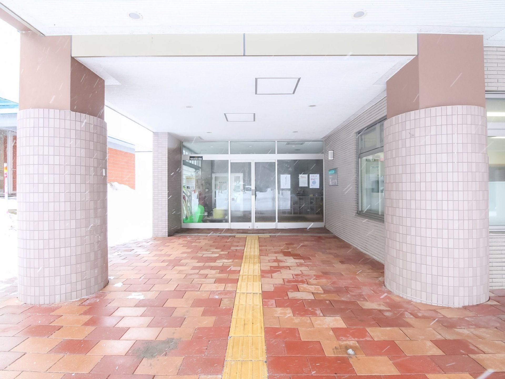 玄関は奥まった場所にあり、２本の円柱の向こうに見えるガラス張りのドアである。玄関への道にはパズルのようにタイルが敷かれている。