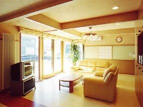 ソファの応接セットが置かれた共有スペースにはテレビもあり、壁一面が大きな窓となっていて大変明るい。壁には時計がかけられ、観葉植物もある。