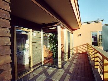 広いテラスにはフェンスが付き、左側にあるリビングから出入りができる設計。屋根が付いていて日当たりもよい。特に椅子などは置かれていない。