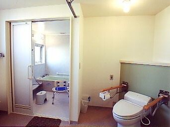 浴室の脱衣所スペースにトイレが設置されている。トイレの両サイドに手すりがあり、浴室にはシャワーチェアやシャワーもある。
