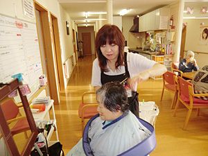 プロの女性美容師にヘアカットをしてもらっている女性入居者。