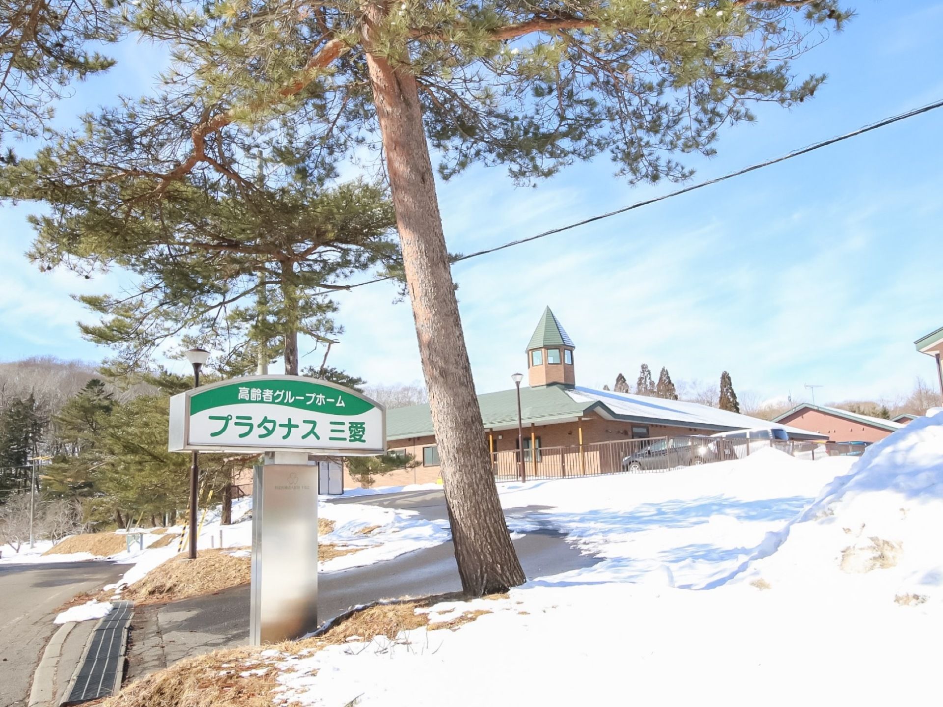 敷地の入り口に施設名を表示した看板が設置されている。周りには木々が植えられており、自然豊かな環境になっている。