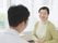 医師とその話を聞く女性の写真。医師は背中を向けて女性がこちらを向いている様子
