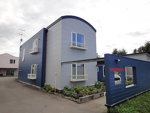 敷地内にはたくさんの植物が植えられ、駐車場もある。ブルー系の2階建ての建物は楕円形の屋根がある。