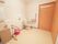 個室トイレの写真で、右奥に入口扉がある。中央に温水洗浄便座があり、壁や便座横に手すりが設置されている。