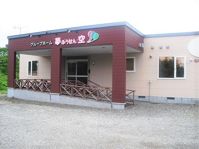平屋建ての建物の玄関部分には手すり付きのスロープと屋根が付き、屋根にはホーム名が書かれている。