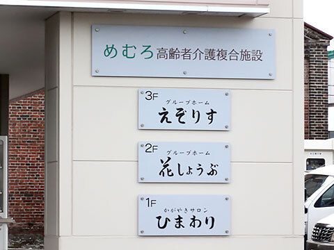 １～３階にそれぞれ違う名前が書かれている。複合施設となっていて、奥には車が複数台止められた駐車場がある。