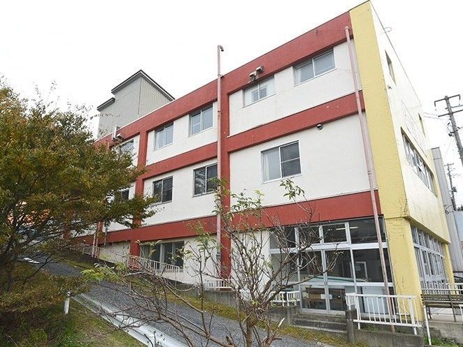 ３階建ての大きな建物。白を基調とし、赤いラインが入っている。