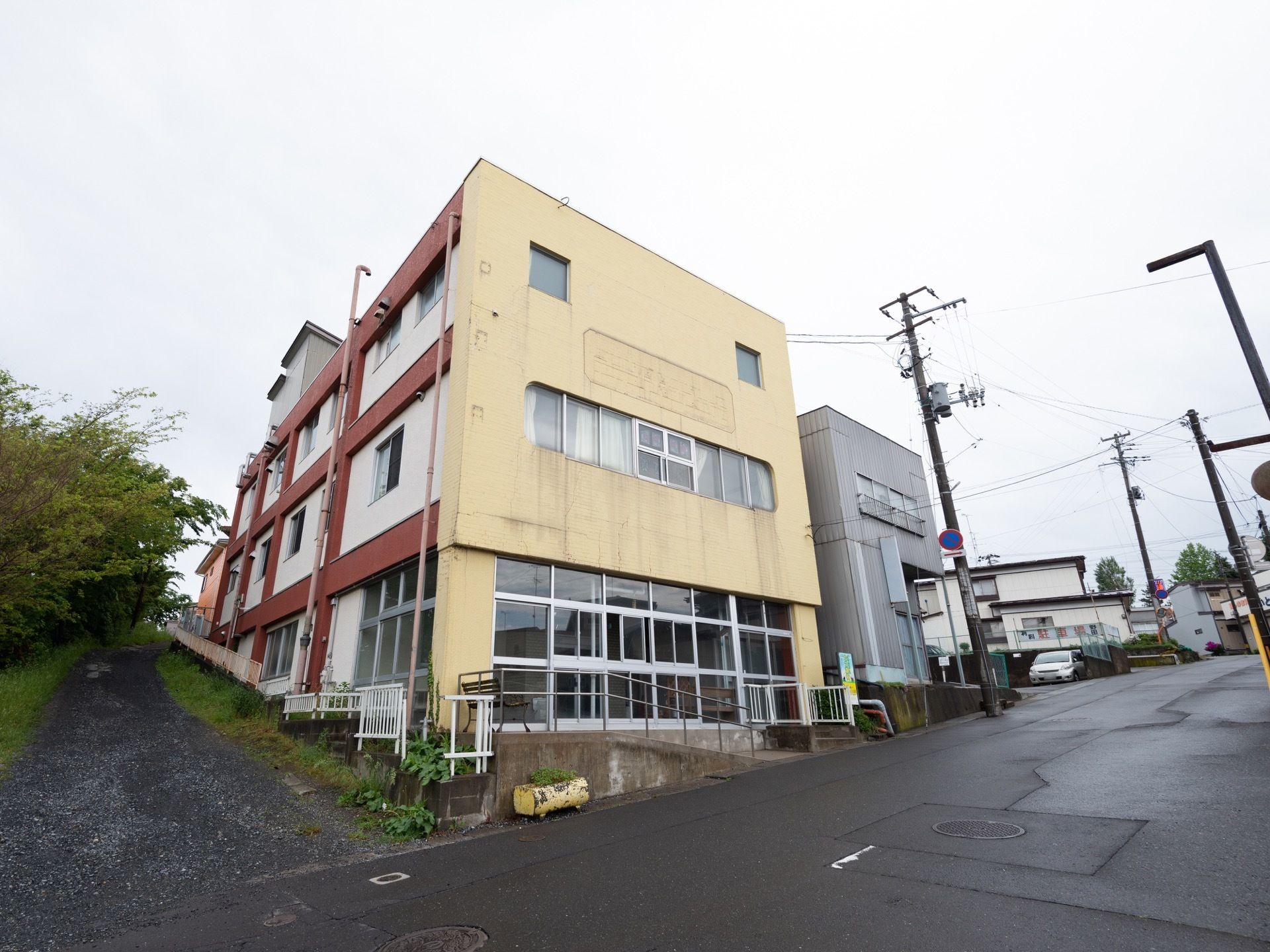 薄黄色と赤色、白色の外観である。入口前にはスロープが設置されており、車椅子をご利用の方でも出入りしやすくなっている。