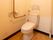 白色の壁で囲まれた空間に、白色のトイレが設置されている。便座右側の壁にはＬ字型の手すりがある。便座周りには広いスペースが確保されている。