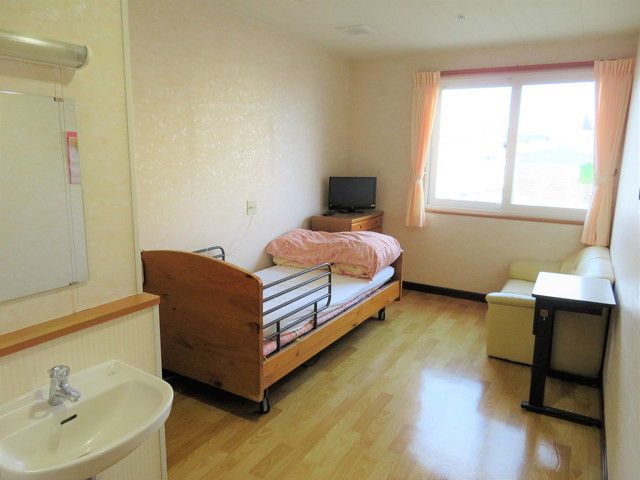 大きな窓が付いた居室にはシーツがセットされたベッドとテレビ、収納家具が付いている。