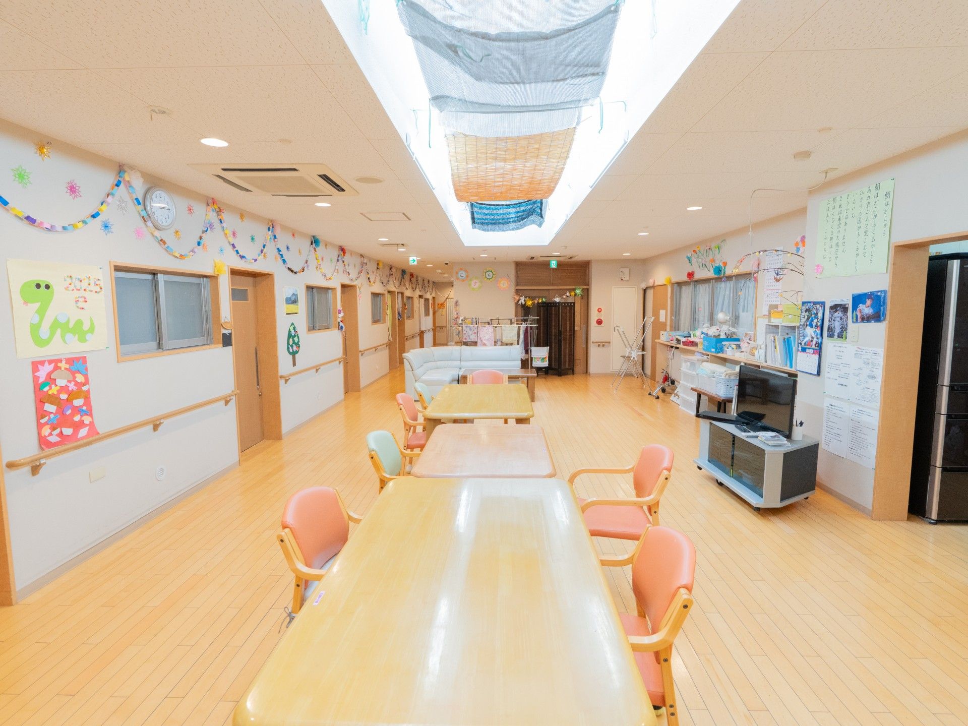 水の入ったコップを持っているエプロンを付けた女性スタッフが笑顔で薬を飲もうとしている高齢女性のそばにいる。