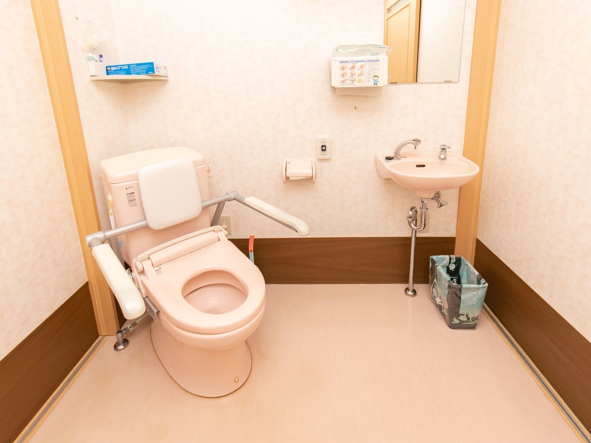 便座の背面がトイレ内の角に向くよう、斜めに設置されている。便座には背もたれや手すりが備え付けられている。