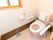個室トイレの画像である。左上に茶色い窓枠の小窓があり、閉めたままになっている。右側に薄いピンクの便座がある。
