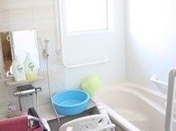 家庭的なサイズの浴室の様子。シャワーチェアや立ち上がり用の手すりが付いている浴室