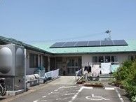 手前に駐車場スペースがある施設の外観。天気が良い日にグループホームひまわりを写した写真。