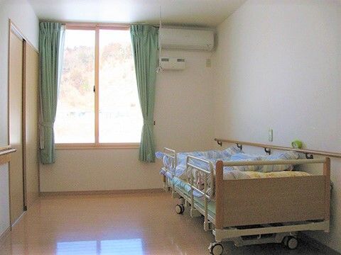 窓がある施設内の居室の様子。エアコンや介護用ベッド、収納がある部屋の写真