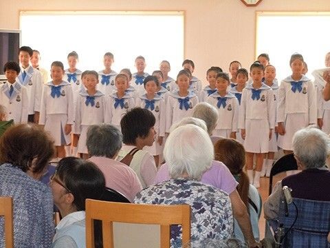 子供たちが歌っている様子を見ている高齢者の様子。スタッフと会話している様子