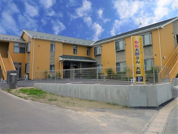 エル字型の２階建ての建物。広い駐車場が付き、フェンスで囲まれている。