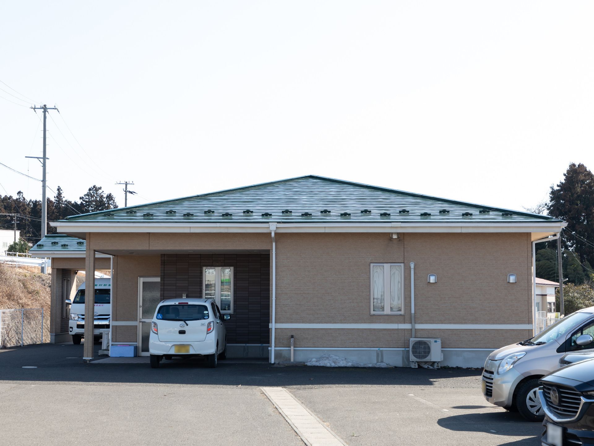 周囲には緑が多くあり、ベージュの外壁の建物は平屋建て。玄関には車寄せが付いている。