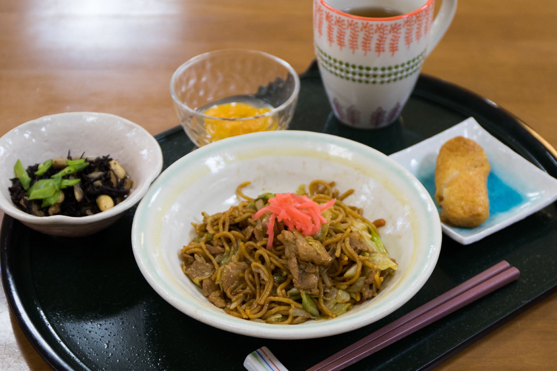 ひじきの煮つけ、焼きそば、稲荷寿司、デザートなどが置かれたトレー