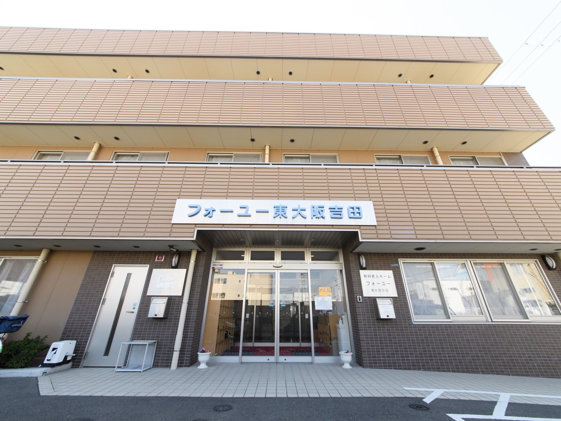 玄関の正面から、施設の外観を写したものである。ガラス張りの自動ドアの上に、大きな文字で施設名が書かれた看板がある。