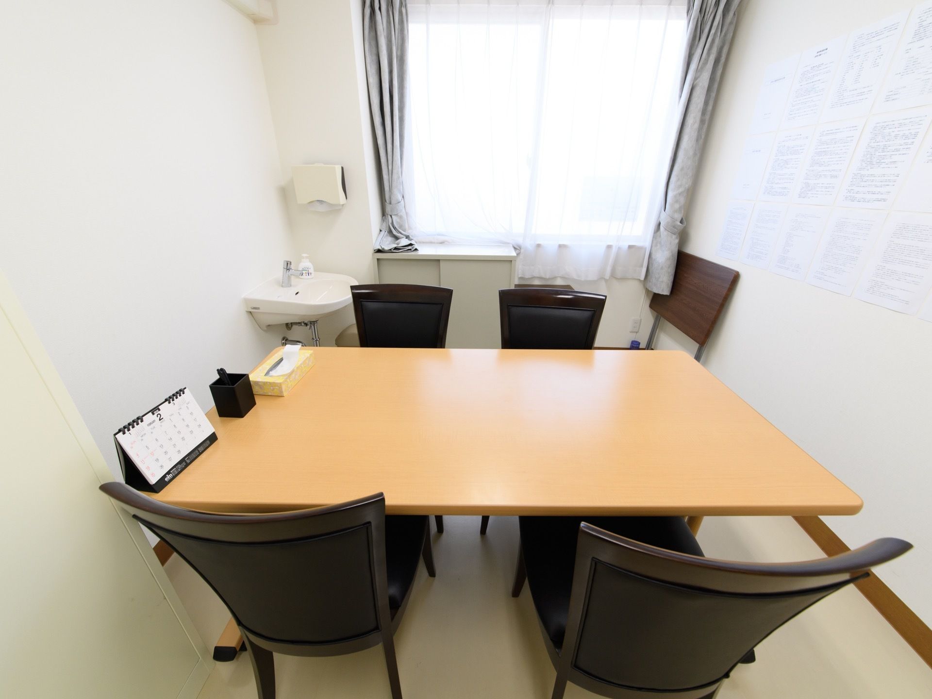 テーブルの左端に、カレンダー、筆記用具、ボックスティッシュが置いてある。壁際には洗面台があり、ハンドソープも用意してある。