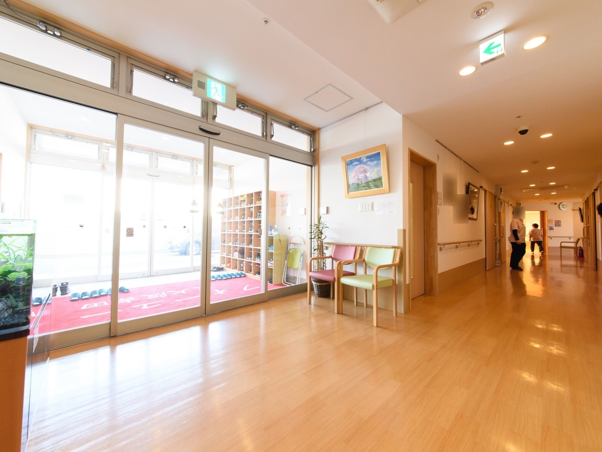 明るく広々としたエントランスホールの壁際に、ピンクとグリーンの２脚の椅子が置いてある。その上に、大きな絵が飾ってある。