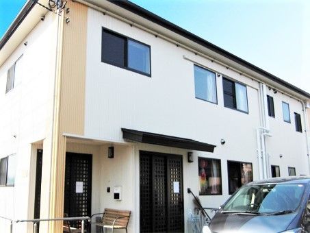 2階建ての建物は白をメインとしていて、玄関には屋根が付き、ベンチも置かれている。