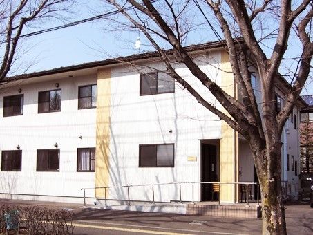 白をメインとした2階建ての建物。玄関部分には手すり付きのスロープが付いている。