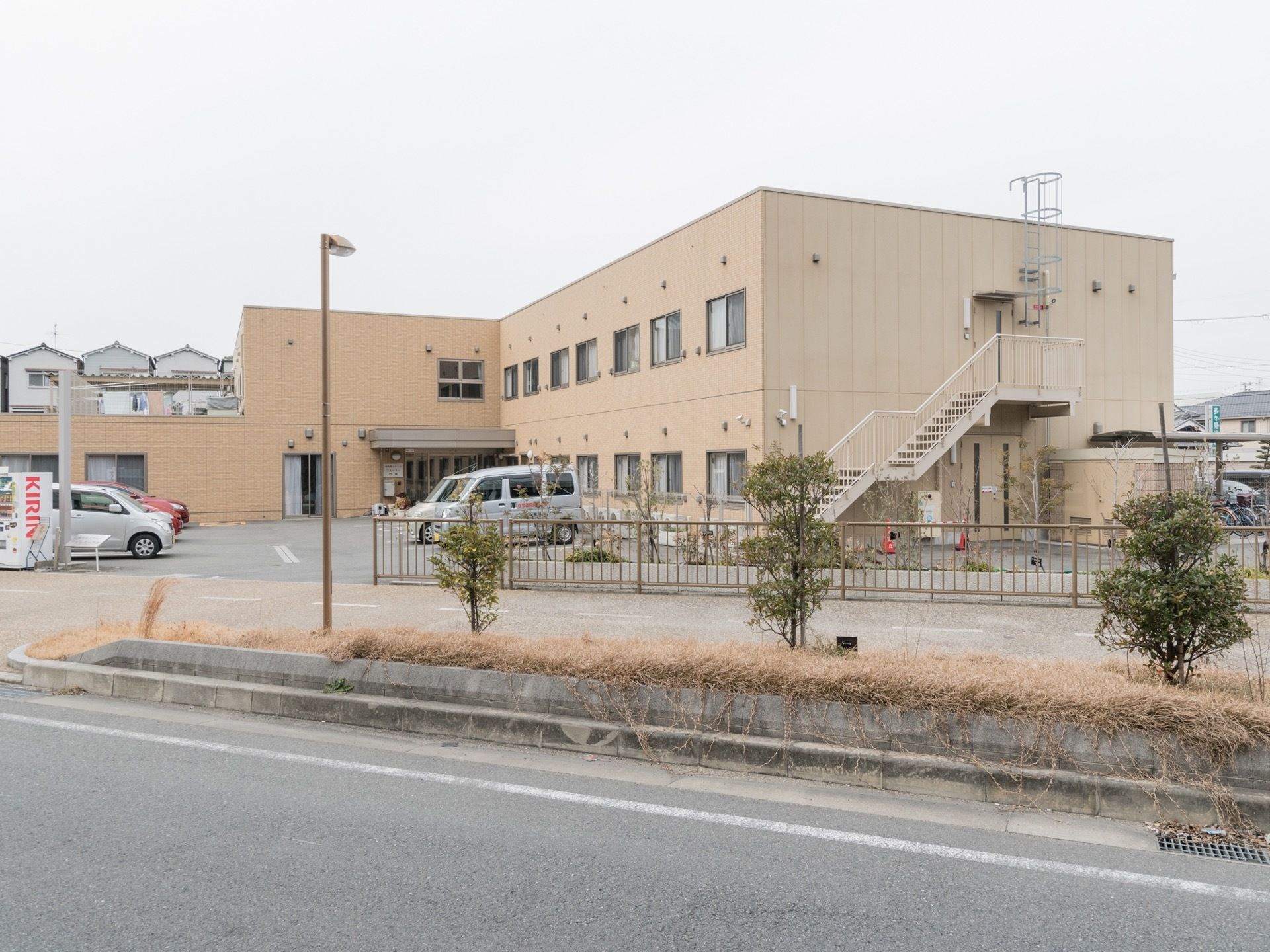 施設には外階段が設置されている。まわりに駐車場、駐輪場が設置され、敷地と道路はフェンスで仕切られている。
