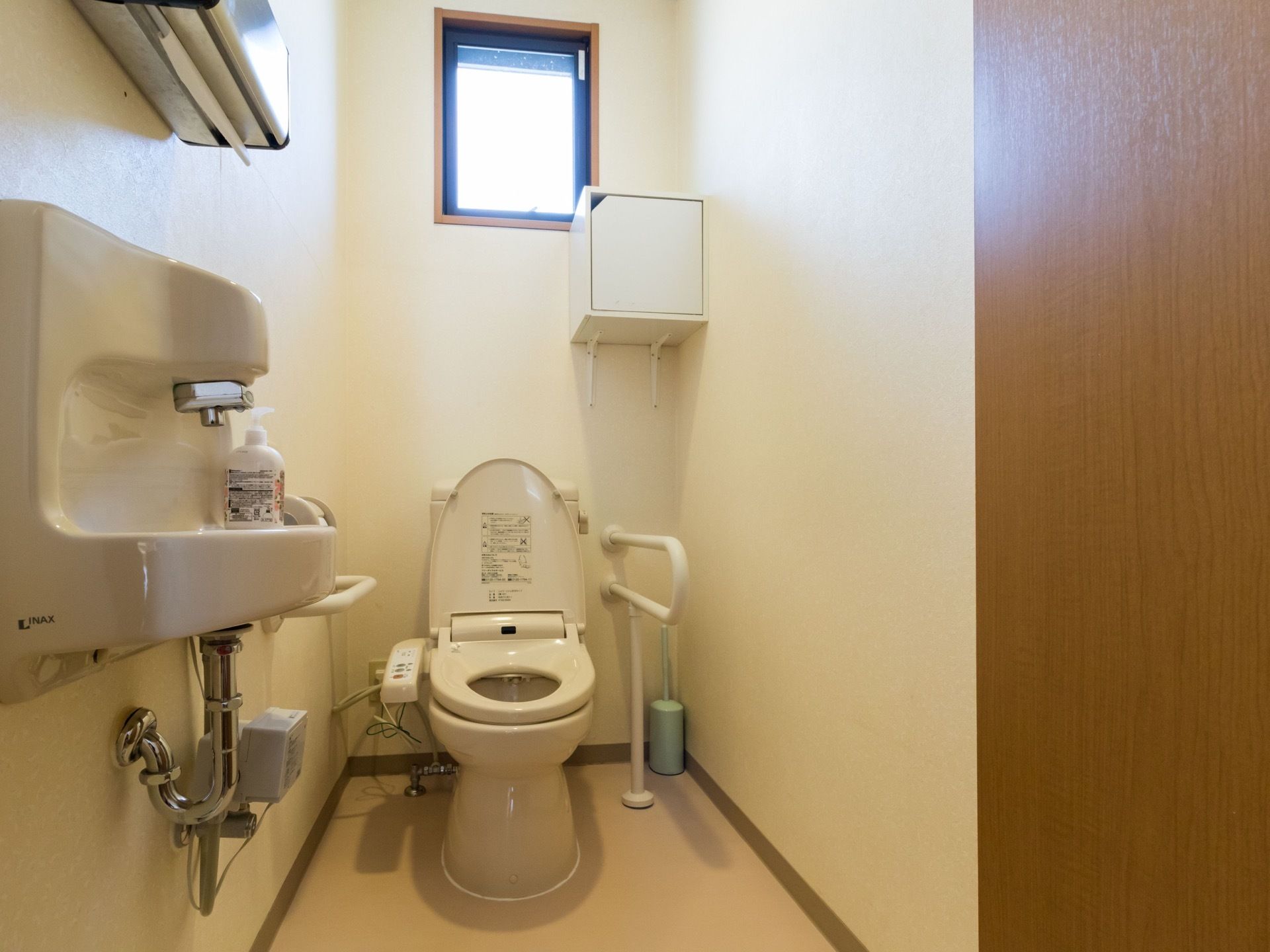 トイレには洋式便器があり、両側には手すりが設置されている。手洗い器のところにはペーパータオルが用意されている。