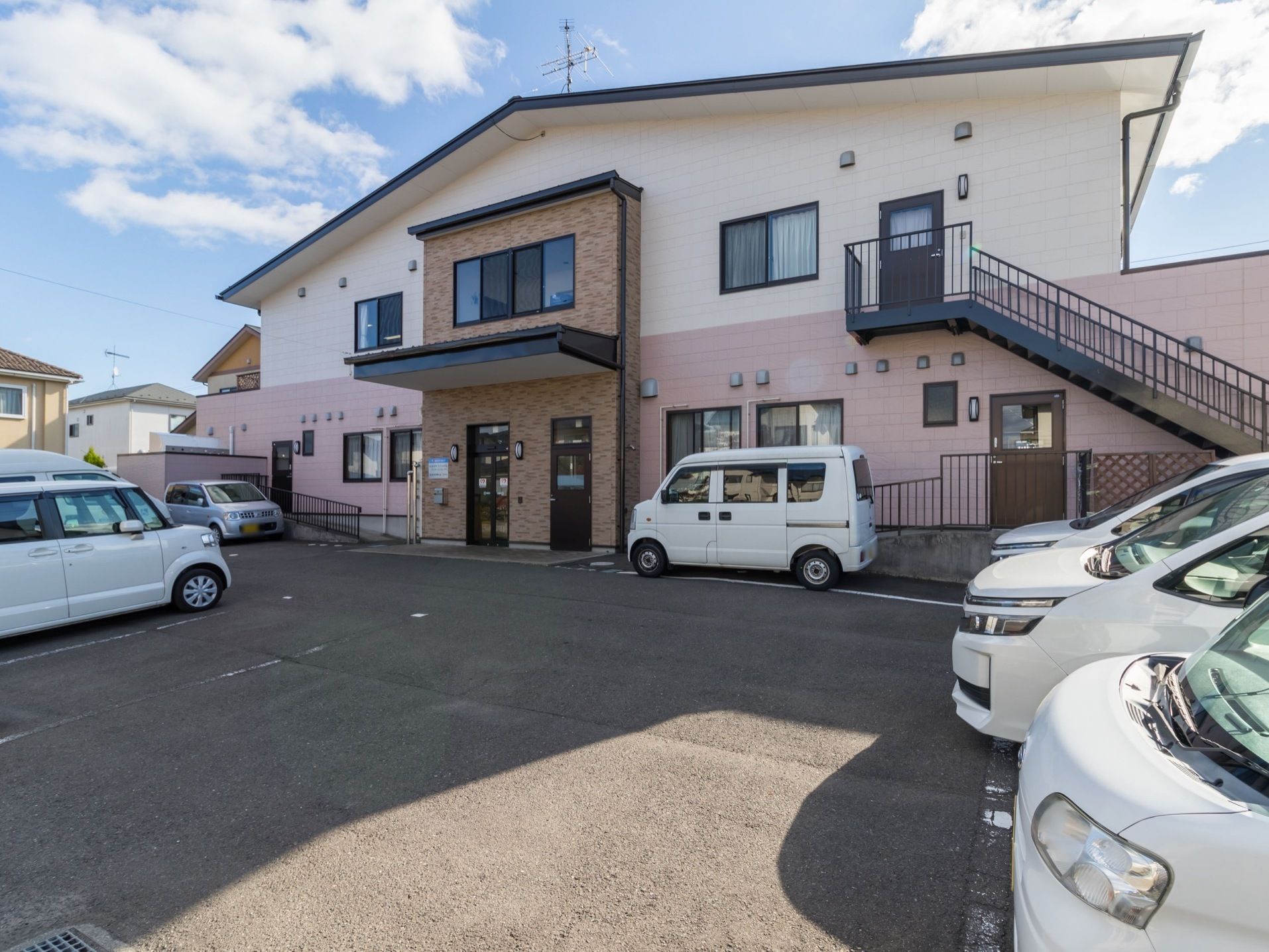 建物の前に、多くの駐車スペースを備えている。施設は２階建てで、戸建てのような家庭的な外観である。玄関ポーチがある。