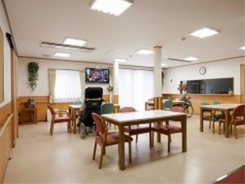4人掛けテーブルセットがゆったりと設置されている食堂である。車椅子をご利用の方がテレビをご覧になっている。