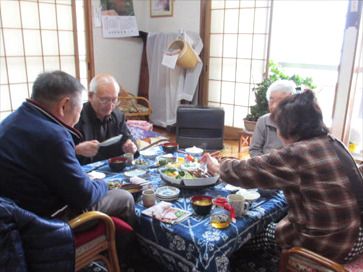 テーブルクロスがセットされたダイニングテーブルを囲んで食事をしている高齢者4名。