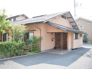 三角屋根の建物。和風の庭が付き、玄関には屋根が付いている。