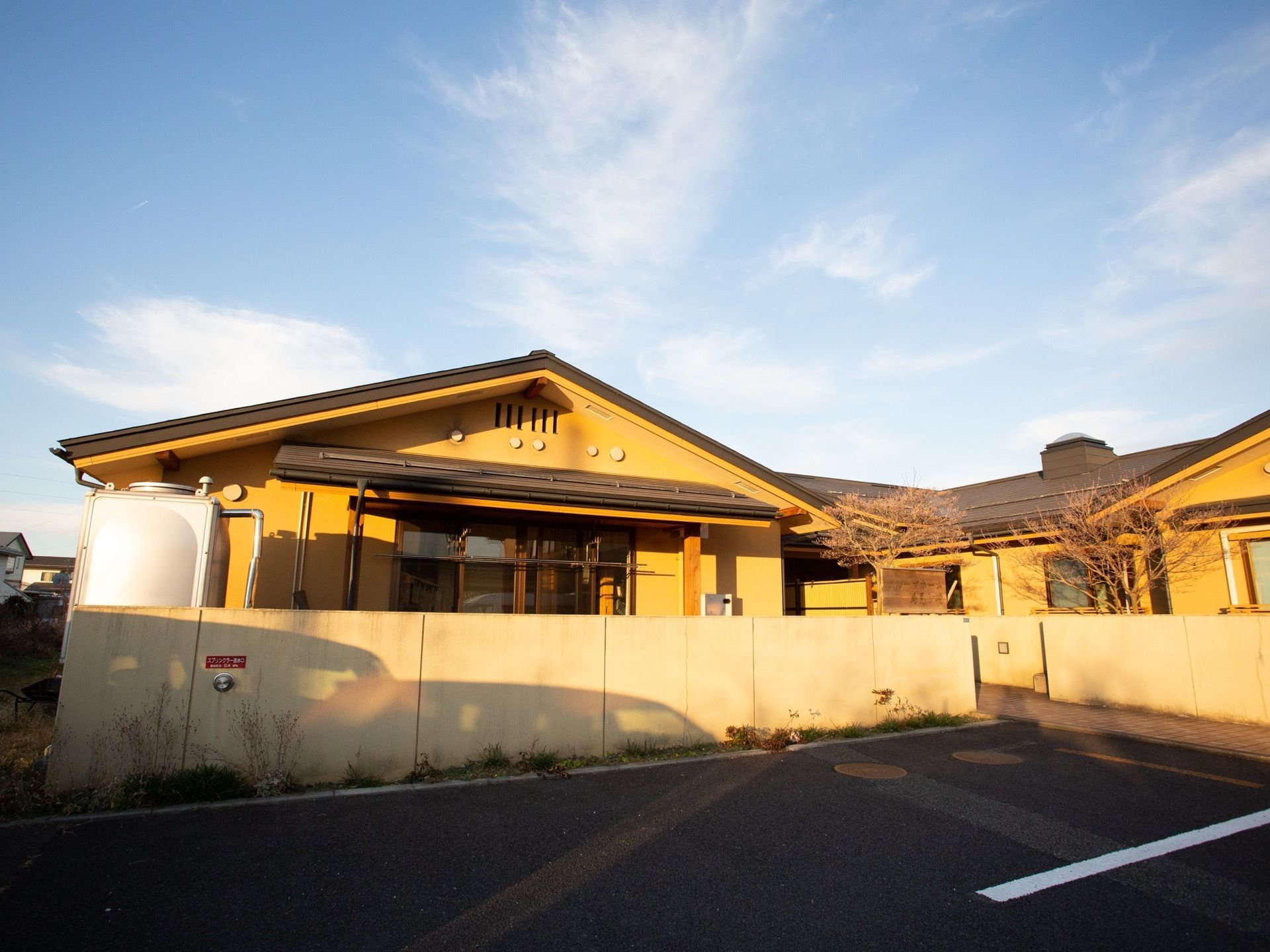施設は黄色の外壁で、三角の屋根になっている平屋建ての建物である。建物の前に大きな駐車スペースが確保されている。