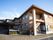 ベージュの外壁の２階建ての大きな建物がある。四角と丸い窓が付いている。敷地内の地面はタイルで覆われている。