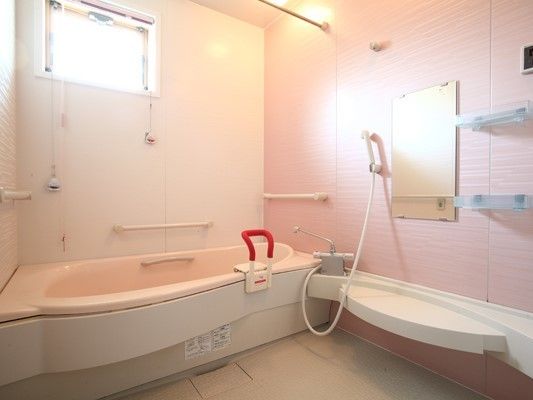 家庭サイズの浴槽が設置されている明るい浴室内には手すりやシャワー、鏡もある。