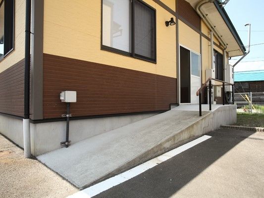 平屋建ての建物の側面にあるドアに続くスロープや手すりが付いている。