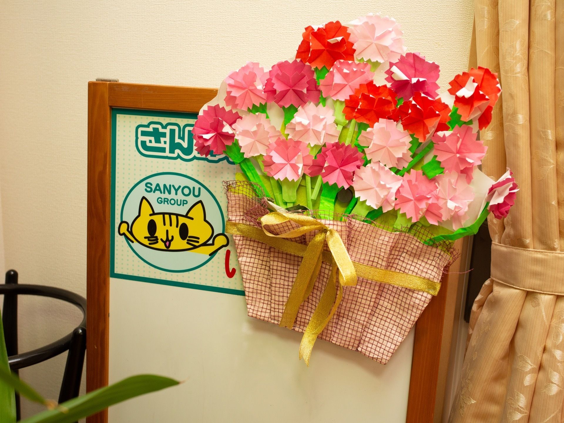 壁際のカーテンのそばには、カーネーションの花束の作品が飾られている。赤やピンクのカーネーションの花が折り紙で丁寧に折られている。