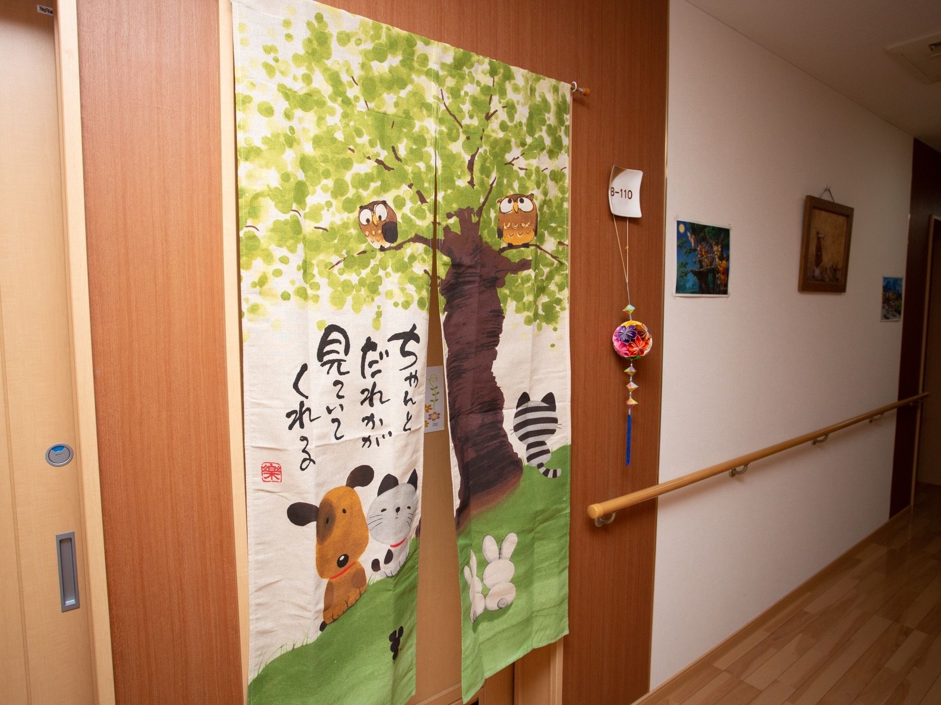 右奥に向かって廊下が真っ直ぐ伸びている。中央に引き戸扉があり、動物や木のイラストが描かれたのれんが下がっている。