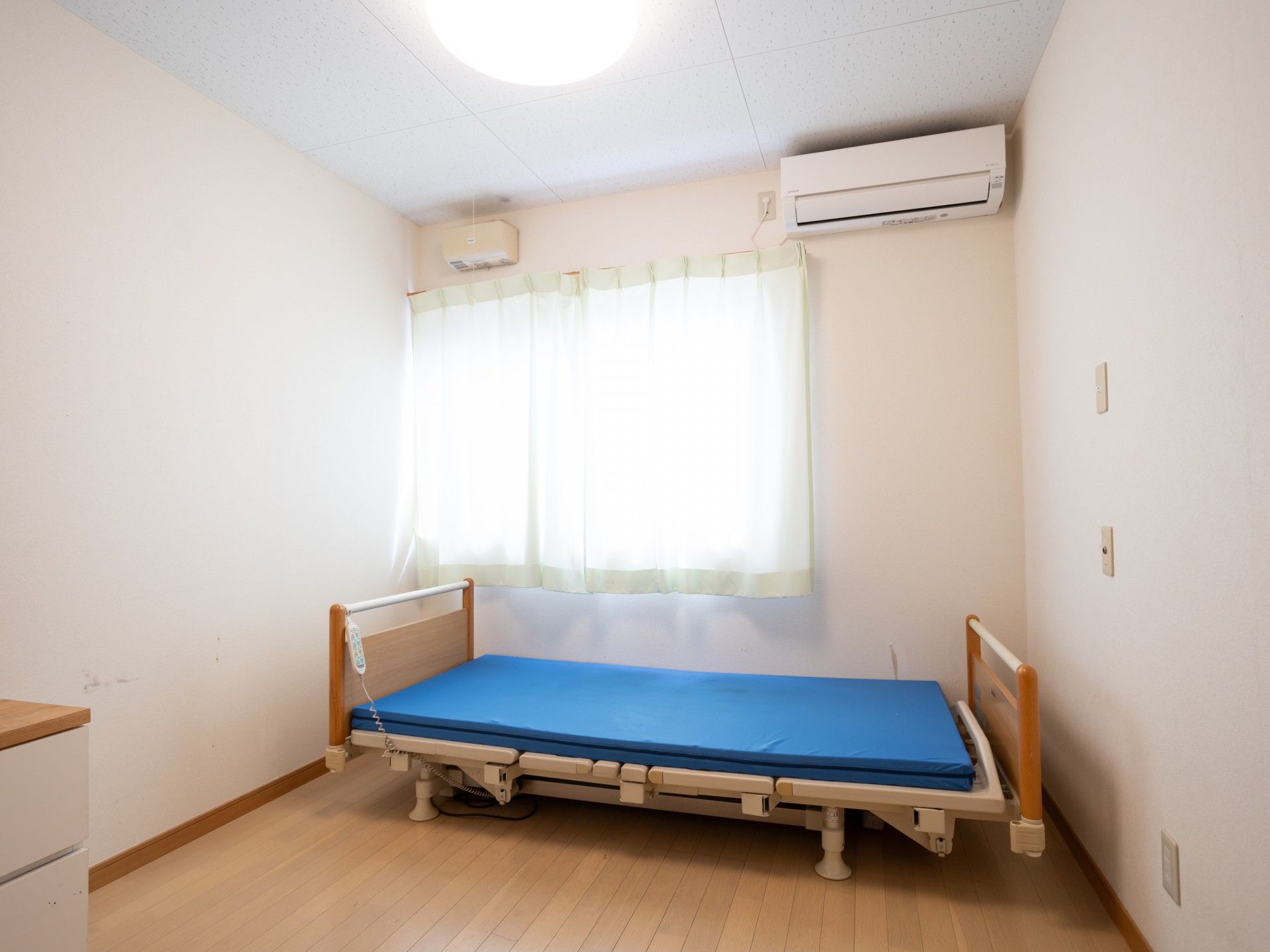 民家の見える屋外で過ごしている車いすの高齢男性と付き添いの若い女性スタッフ。スタッフはブルーのポロシャツを着ている。