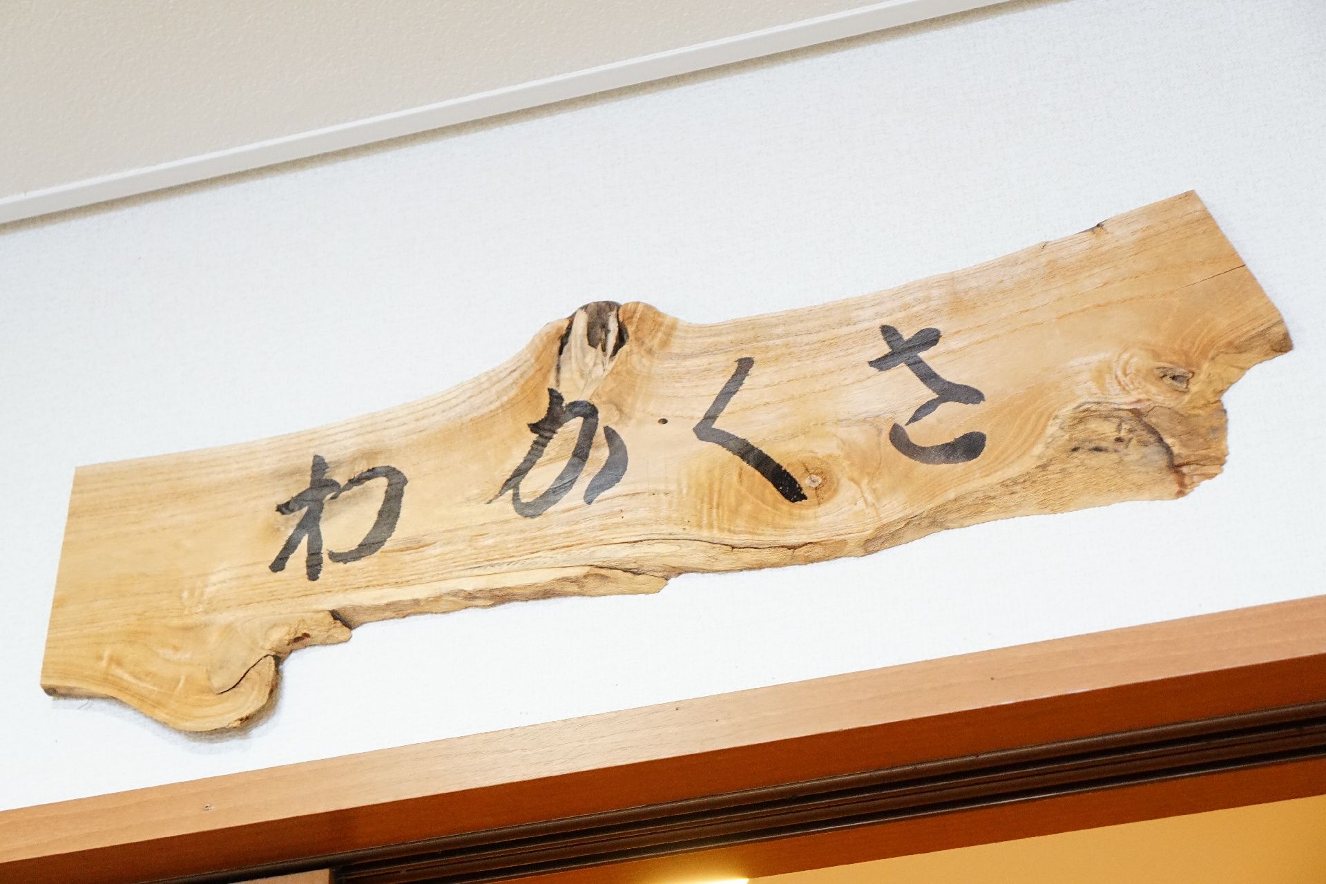 共有スペースの部屋の名前が墨で書かれている木の看板