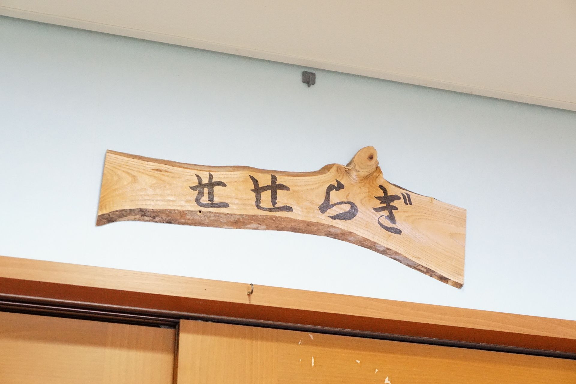 共有スペースである部屋の名前が墨で書かれている木の看板