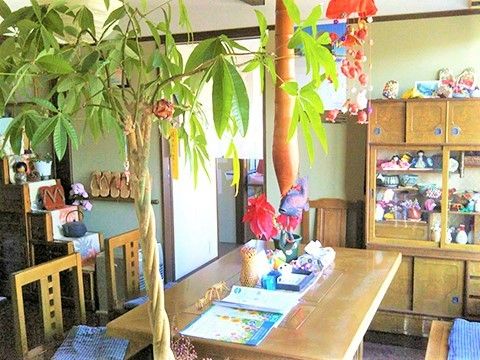 民芸品がたくさん飾られたスペースには木製のダイニングテーブルや観葉植物やが飾られている。